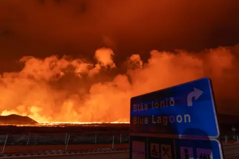 A road sign for Blue Lagoon with flames in background 