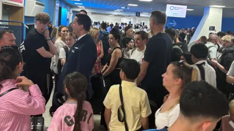 BBC A large group of passengers at Birmingham Airport baggage reclaim