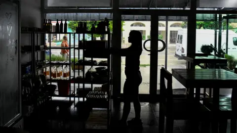 Reuters Seorang wanita bekerja di sebuah restoran saat listrik padam di Havana, Kuba. Dia berada dalam bayangan dan sedang melihat sesuatu di rak rak.