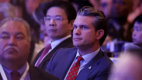 Getty Images Us Defesa Secretário Pete Hegseth sentado em uma multidão ouvindo o discurso de Emmanuel Macron, enquanto o primeiro -ministro de Cingapura Lawrence Wong é visto em segundo plano