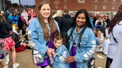 Lauren Stephenson with her daughter, Florence, and Brinda Selvamanoharan, smile at the camera amongst a crowd at Anfield Stadium