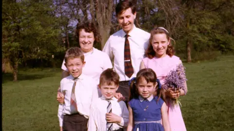 Julie Stevenson Mr and Mrs Stevenson, with four children in front of them, with everyone looking into the camera.