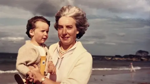 Supplied Alex Morgan as a child being held by her mother on a wind-swept beach. Both are wearing a cream cardigan and their hair is blowing in the wind.