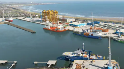 An aerial view of the port of Blyth with a number of docks visible and ships moored up. Beyond the port the coast stretches out.
