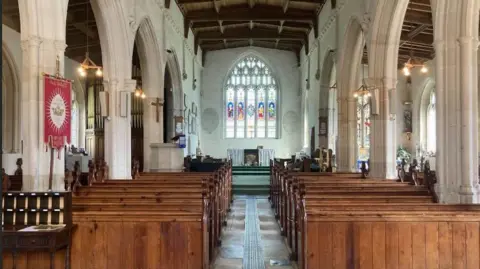 A Shearman Interior of church with pews and large stained glass window on rear wall.