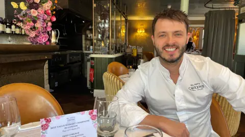 A man in a white shirt is sitting in a restaurant at a table