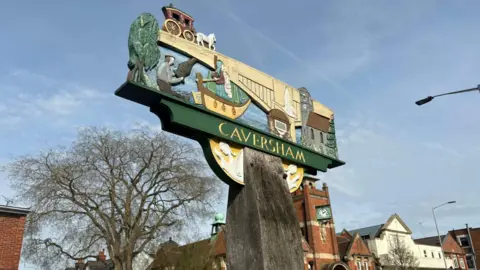A Caversham sign with an artistic village scene depicted on it.