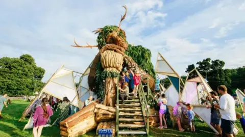 Nici Eberl Families and children explore a large sculpture of a Green Man.