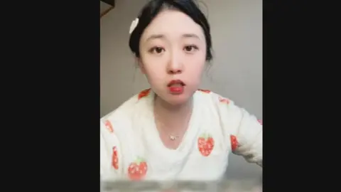 Chinese social media A young Chinese woman called Li Yixue looks in the camera, wearing a white top with strawberries decorating it, red lipstick, and her hair tied back and held by a slide.