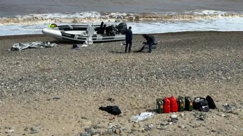 A small inflatable-type boat abandoned at Easington beach, close to the sea, with cannisters lined up in a row closer inshore