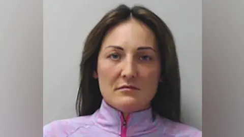 Police Scotland Alisha Bain, a woman with long dark hair and wearing a pink/purple zip top, staring at the camera, unsmiling, in a police mugshot.