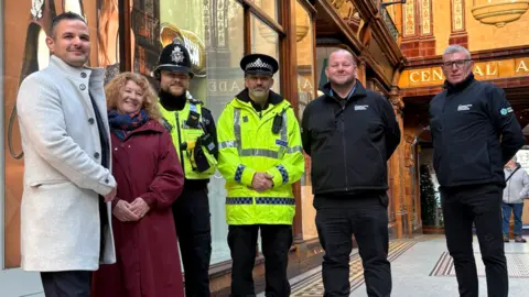Northumbria Police Northumbria Police and Crime Commissioner Susan Dungworth is standing in an old-fashioned looking shopping arcade with police officers, retailers and security guards. 