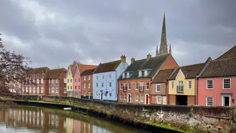 Walking Tractor / BBC Weather Watchers Norwich's colourful Quayside along the River Wensum, where several homes painted different colours, including pastel blue, yellow and pink, line the river, with the cathedral's spire in the background