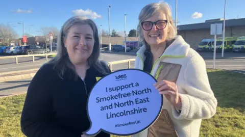 Two women holding a sign standing in hospital grounds