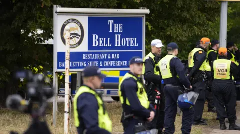PA Media A group of police in high-vis vests stand outside a sign for The Bell Hotel in Epping.