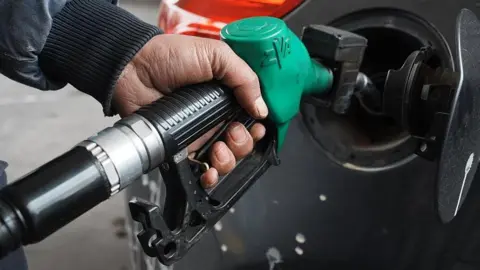 A man topping up his car's fuel using a green petrol pump