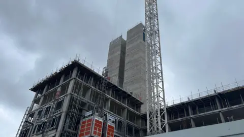 Two tall grey structured are pictured in a building site next to a large crane