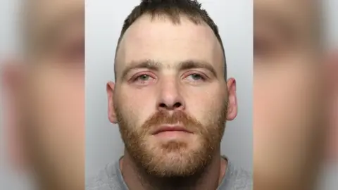 Polisi Yorkshire Barat Gambar tahanan Mark Ross. Dia memiliki janggut merah pendek dan memalingkan muka dari kamera. 