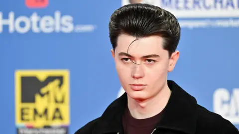 Elliot James Reay poses for photographers against a blue branded backdrop at the MTV Europe Music Awards in Manchester in 2024.