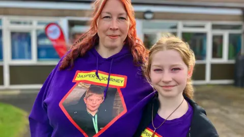 Nicola Rees/BBC Kim Cook with her daughter Lily, both wearing purple tops with photos of Jasper on, which say 'Jasper's journey'