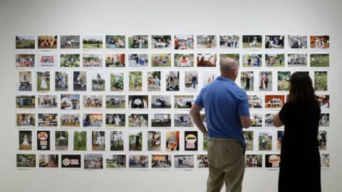 National Trust A man and a woman standing in front of a wall of photographs, with their backs to the camera. 