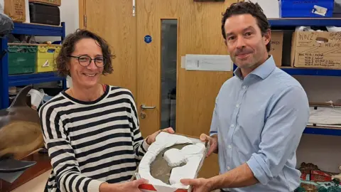 A wide shot of a woman and Xavier Duffy holding the astrolabe.