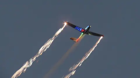 Matt Judge/BBC Aircraft with sparks flying from its wings and 2025 and a heart lit up under one wing