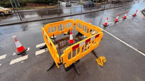 The covered over sinkhole with yellow barriers around it.