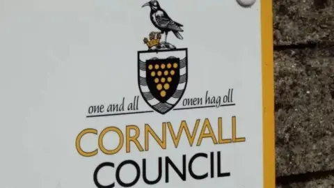 BBC A large white sign for Cornwall Council, including the council logo and motto, "one and all", written in both English and Cornish