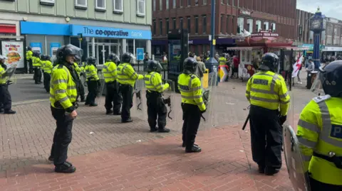 A line of officers in helmets and with shields stand in the centre of Hanley