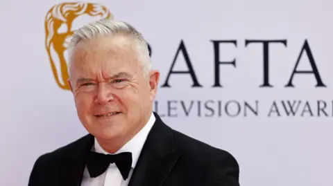 Huw Edwards in a bow tie standing in front of a Bafta logo