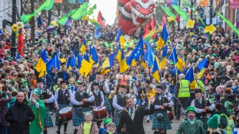 Martin McKeown A huge crowd of people make their way down Shipquay Street in Derry. The city's mayor is at the front, a pipe band just behind. Flags are being flown