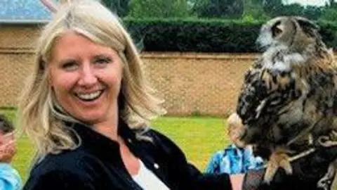 FAMILY HANDOUT Joanna smiling at the camera holding an owl on her hand. She has blond shoulder-length hair and is wearing a white top with a black shirt.