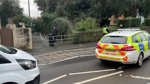 Police car and officers outside the park entrance. A police cordon can be seen on the gate.