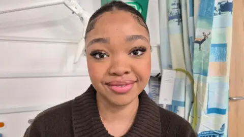 A picture of a young woman smiling at the camera while sitting in a hospital room