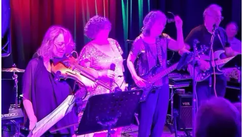 Silhouette Band The band perform on stage under pink lighting. 