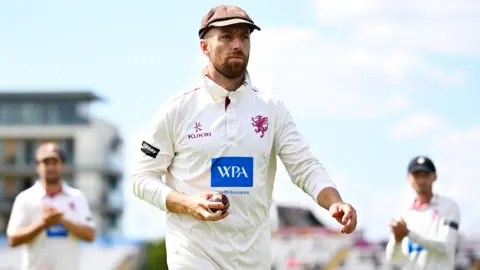 Jack Leach walks off the outfield at Taunton holding the ball in his right hand