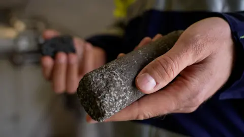 A man holds a cylindrical piece of black Icelandic stone with trapped white carbon