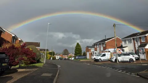 Shanedeep Sandhu A rainbow curves over a street with homes on either side.