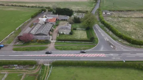 An aerial view of Charlton Mires which is a large Georgian farmhouse surrounded by farm buildings with a cottage visible in the background and the A1 in the foreground