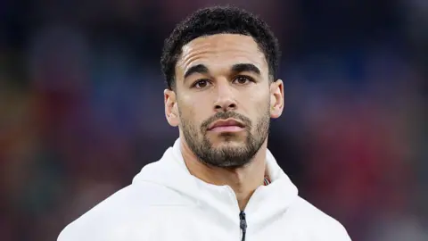 Ben Cabango. It is a head shot of a man looking at the camera. He has a white zipped top. The background behind him is blurred.