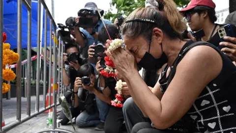 AFP via Getty Images A woman prays for her deceased daughter and her son-in-law Suwitcha Sirililung in front of the Rong Beer Na Lat Phrao bar in Bangkok on July 14, 2026.