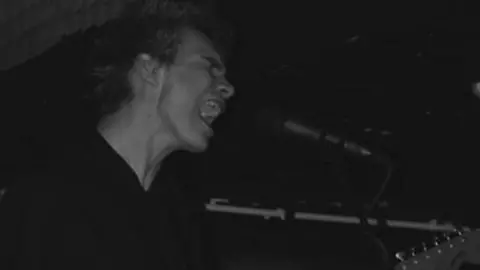 Oliver Ripley A black and white picture of a young man singing into a microphone