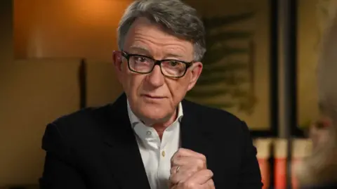 Lord Mandelson rubbing his hands together anxiously in a BBC studio