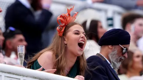 PA A woman leans over the railing to cheer on the horses during Ladies Day at Aintree