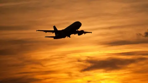 Getty Images A silhouetted plane takes off during a sunset. 