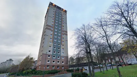 Google Un gran bloque de pisos en Motherwell con árboles desnudos afuera en un día gris y nublado.