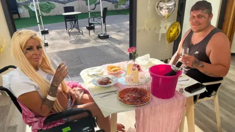 Two people sat at a table with pizza, spaghetti bolognaise and bubbly in a pink bucket. 