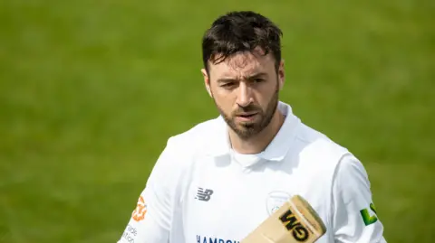 Hampshire cricket captain James Vince wearing cricket whites and holding a cricket bat