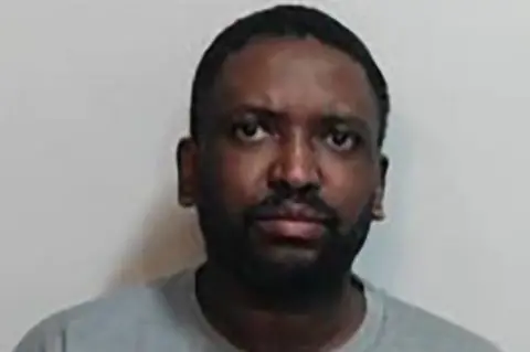 Police Scotland Isaacs has a black moustache and short black hair. He is wearing a grey t-shirt.